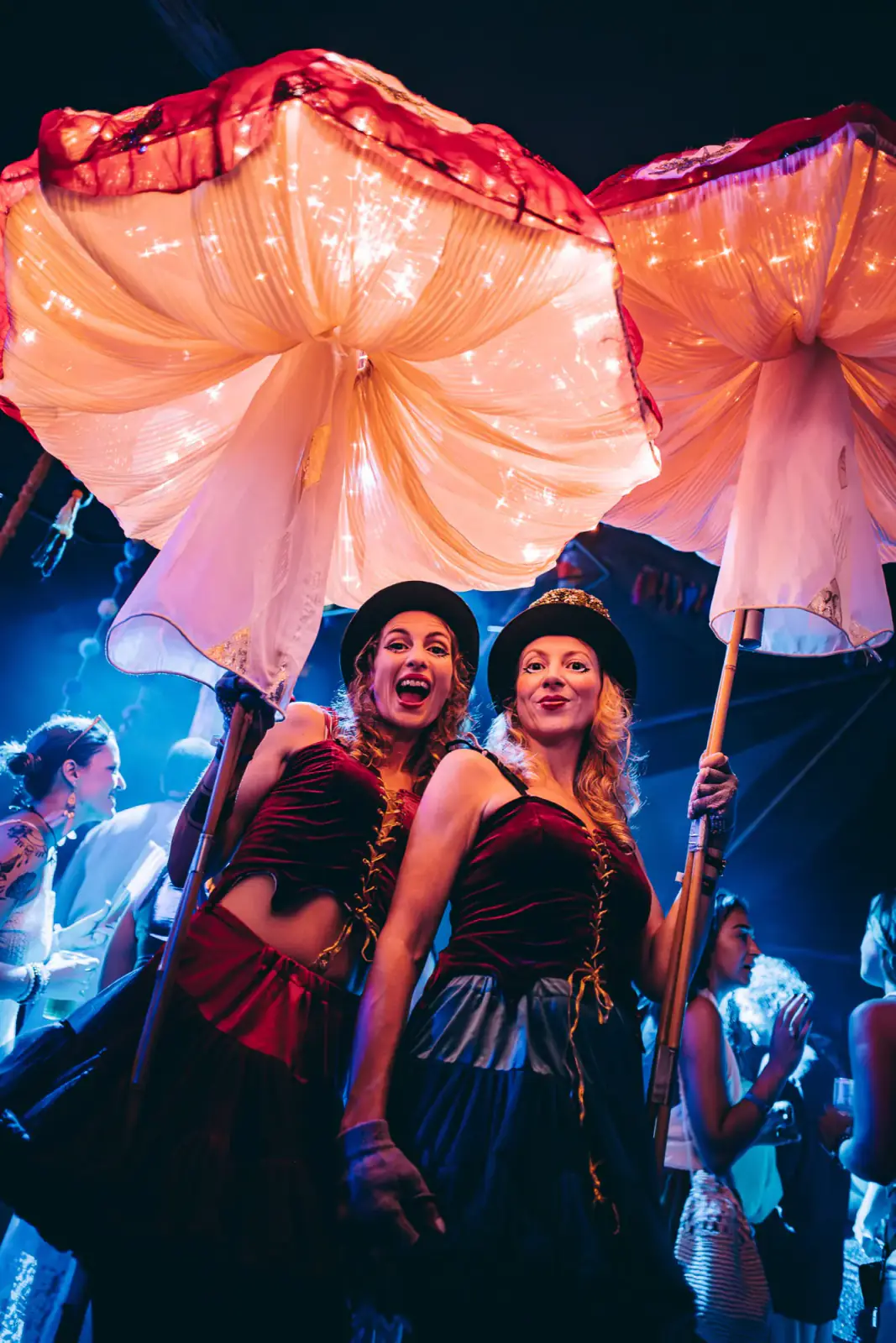 Performers carrying glowing mushroom parasols through the night crowd
