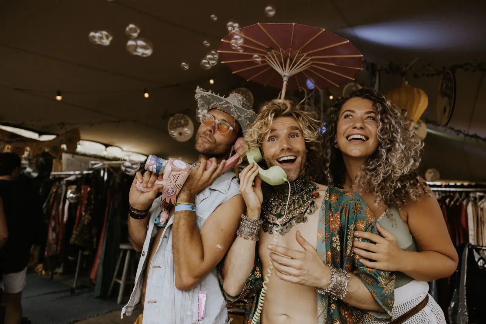 Three friends sharing vintage telephones under a parasol while bubbles drift by